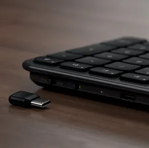 Satechi slim kabellose Tastatur in Schwarz mit Mac-/Windows-Umschalter und USB-C-Empfänger auf Holzoberfläche.