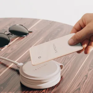 Satechi FindAll Wallet-Karte in Creme, über einem passenden Ladeetui auf einem Holztisch gehalten.