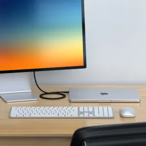 Satechi Thunderbolt 5 Pro kabelis melnā pītā dizainā, kas savieno monitoru ar aizvērtu klēpjdatoru uz galda