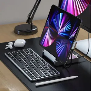 Satechi-alumiininen tabletin Stand Hub -teline, jossa tabletti on tuettuna pystyasentoon työpöydällä näppäimistön ja nappikuulokkeiden vieressä