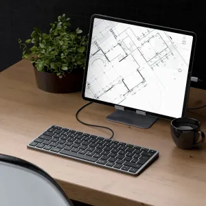 Satechi W1 USB-C-tangentbord på ett skrivbord bredvid en surfplatta, som visar den kompakta trådbundna Mac- och iOS-designen