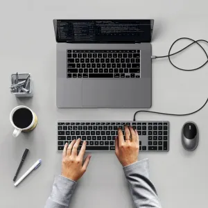 Satechi W3 USB-C-tangentbord med numeriskt tangentbord, anslutet med kabel till en laptop på ett skrivbord medan händer skriver