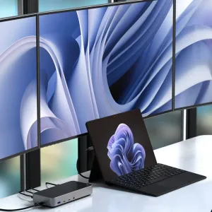 Satechi kolmen 4K-näytön telakointiasema tablettikannettavan vieressä, yhdistettynä kolmeen näyttöön työpöydällä.