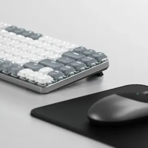 Satechi sM1 tunt mekaniskt tangentbord med grå och vita tangenter, visat vinklat på en ljus bordsskiva.
