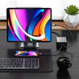 Cargador de viaje Satechi GaN de 100 W alimentando una tableta y un smartphone sobre un escritorio, con puertos USB-C y USB-A.