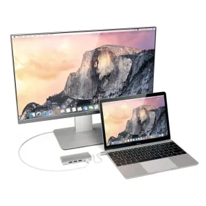 Satechi USB-C kelių prievadų adapteris, sidabrinės spalvos, prijungtas prie nešiojamojo kompiuterio ir išorinio monitoriaus, matomi trys USB prievadai.