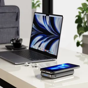 Satechi Duo Wireless Charger Stand lataamassa älypuhelinta pöydällä kannettavan tietokoneen ja nappikuulokkeiden vieressä
