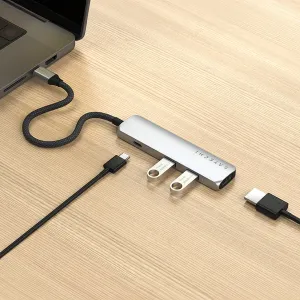 Hopeinen Satechi USB-C -moniporttisovitin liitettynä kannettavaan tietokoneeseen, punottu kaapeli puupöydällä.