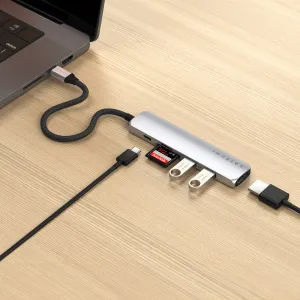Satechi USB-C plānais daudzportu adapteris, kas pievienots klēpjdatoram, ar ievietotu SD karti un pieslēgtiem USB piederumiem.