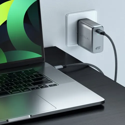 Satechi 100 W GaN USB-C-vegglader i veggkontakt, grå metallfinish, med flettet USB-C-kabel koblet til bærbar PC på skrivebordet.