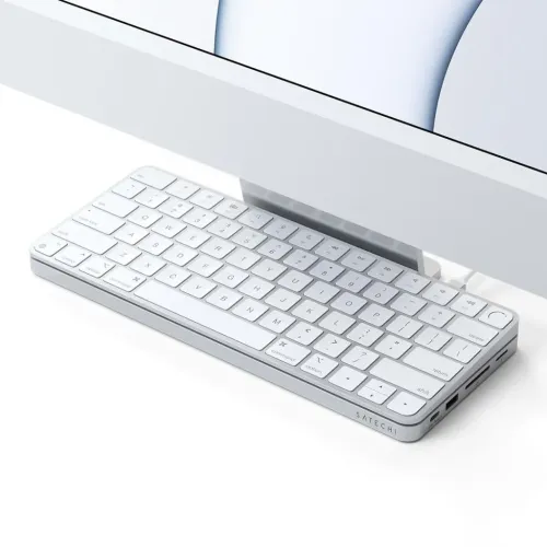 Satechi USB-C Slim Dock in silver under iMac, low profile with ports on the right: USB-C, USB-A, SD and microSD; cable visible.