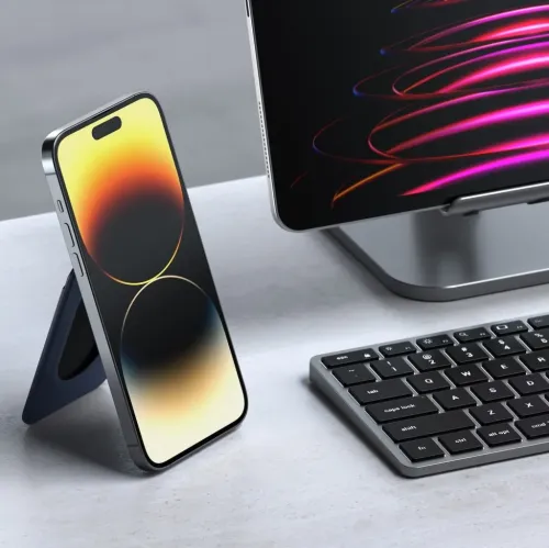 Magnetisk lommebokholder i blått festet på baksiden av iPhone, brettet til trekantform som støtte i stående modus på skrivebordet.