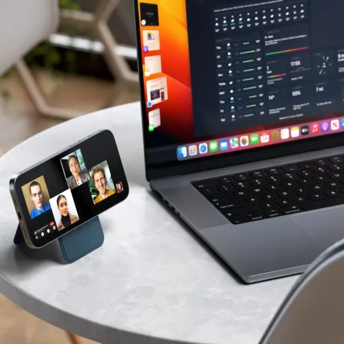 Magnetisk lommebokstativ i mørkeblått vegansk skinn holder en iPhone horisontalt på et bord, plassert ved siden av en bærbar datamaskin.