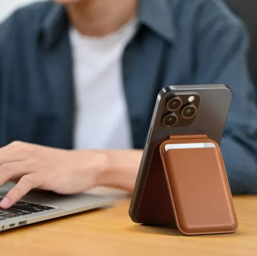 Pungstativ i brunt læder, der er fastgjort til bagsiden af en iPhone, foldet som et stativ med et kort delvist synligt i forlommen.