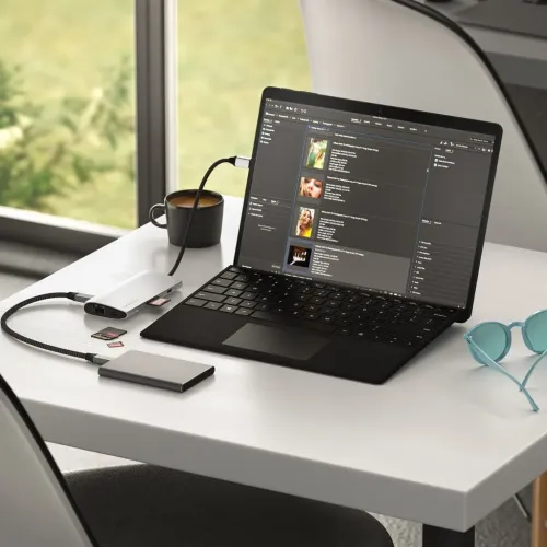 "Satechi" USB-C adapteris pilkos spalvos staliniame kompiuteryje, prijungtas prie nešiojamojo kompiuterio, su Ethernet prievadu, SD kortelių skaitytuvu ir USB-C prie išorinio SSD.