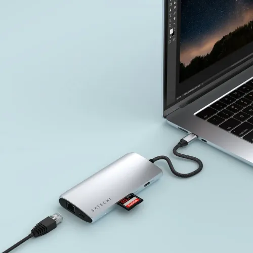 "Satechi" USB-C daugiaportis sidabro spalvos adapteris, prijungtas prie nešiojamojo kompiuterio, su eterneto prievadu, HDMI, USB-C ir įdėta SD kortele šone.