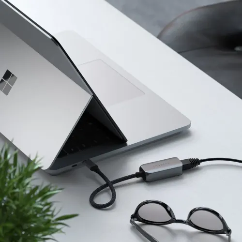Satechi USB-C til Ethernet-adapter i aluminium med flettet kabel, koblet mellom bærbar PC og nettverkskabel på bordet.