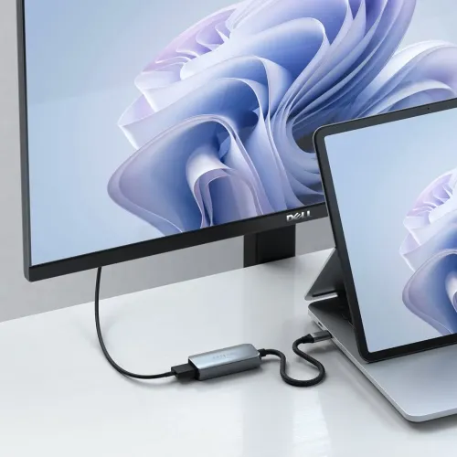 Satechi USB-C til HDMI-adapter i aluminium med flettet kabel, koblet mellom et nettbrett og en stasjonær skjerm.