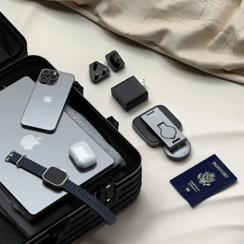 3-i-1 sammenleggbart Qi2-ladestativ i grått, sammenbrettet, med svart USB-C-strømadapter og to reiseadaptere plassert på stoff.