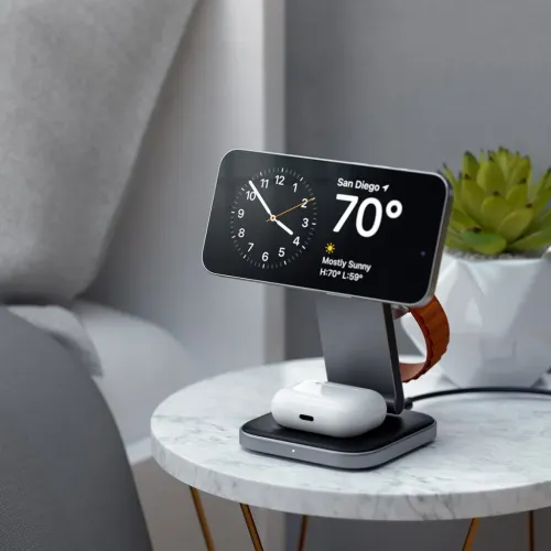 3-i-1 sammenleggbart ladestativ i metall med telefonen horisontalt, AirPods-etui på basen og klokkerem rundt bak på bordet.