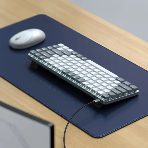 Lysegråt mekanisk tastatur med baggrundsbelysning, på fødder med tilsluttet USB-C-kabel, placeret på blå skrivemåtte.