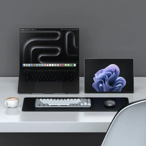 Slank, lysegråt tastatur med hvide og grå taster på bordskåner, lav profil, foran laptop, tablet og mus.