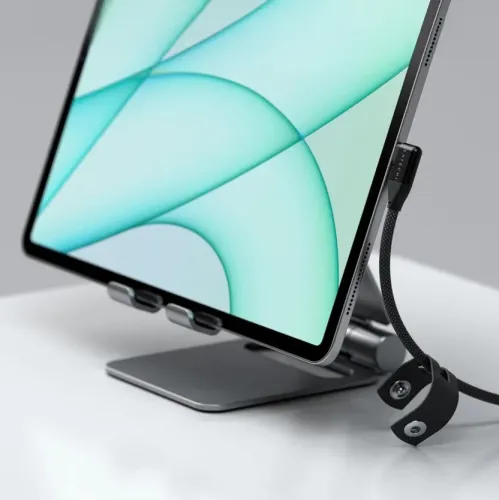 "Satechi" dešinio kampo juodas USB-C kabelis su pinta įmaute, prijungtas prie šoninio planšetinio kompiuterio krašto, su kabelio dirželiu ir lenkta jungtimi.