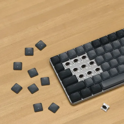 Satechi SM1 Slim tangentbord i mörkgrått på träbord; borttagna tangenter visar brytare, lösa tangentkåpor bredvid och fästen.