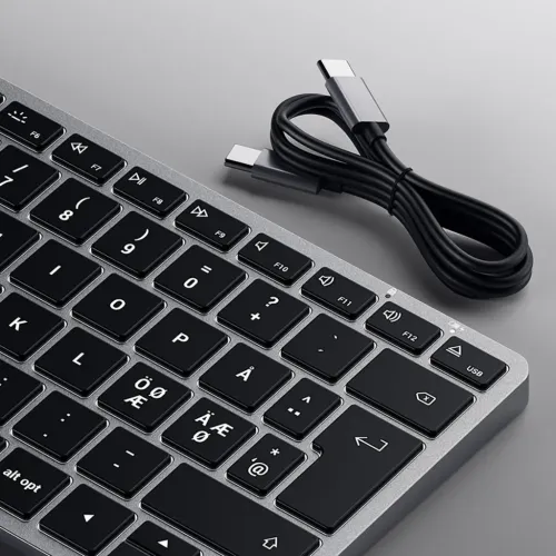Slimmat tangentbord med aluminiumram och nordisk layout i närbild, tangenter med indikatorlampor och en USB‑C‑kabel ovanför.