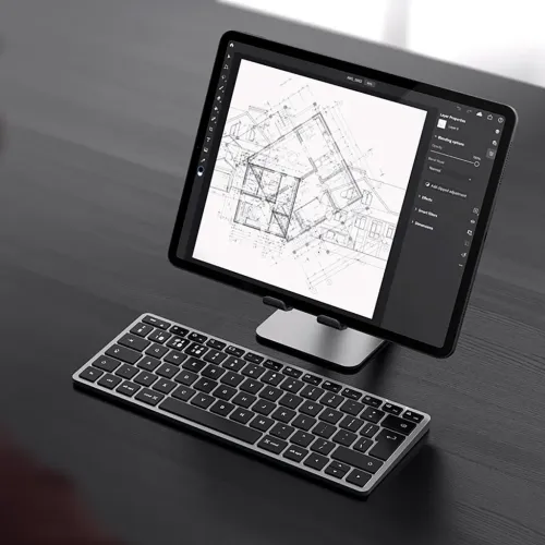 Satechi X1 trådlöst tangentbord i aluminium med låg profil på mörkt skrivbord framför surfplatta på stativ, svarta tangenter.