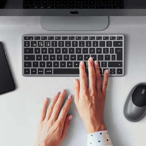 Satechi X1 trådlöst tangentbord i rymdgrått, lågprofil med funktionsrad och piltangenter; händer skriver, mus till höger.