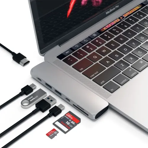 Satechi USB-C Pro Hub i sølv koblet til MacBook Pro, med to USB-A-, HDMI-, SD- og microSD-kortsporskabler ved siden av.