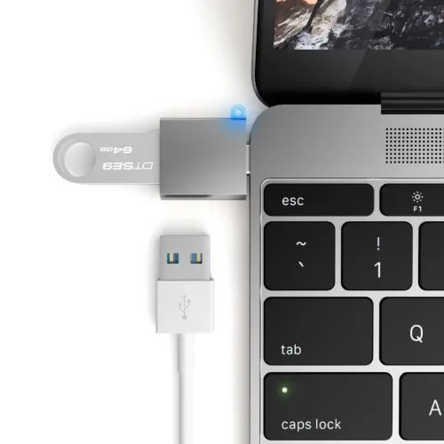 Satechi USB-C til USB 3.0-adapter i space grey koblet til datamaskinens USB-C-port, med USB-minnepinne koblet til og USB-kabel ved siden av.