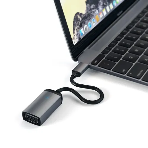 USB-C til VGA-adapter i space grey, med kort kabel og LED, tilsluttet en bærbar computer; VGA-hunport tydeligt synlig på forsiden.