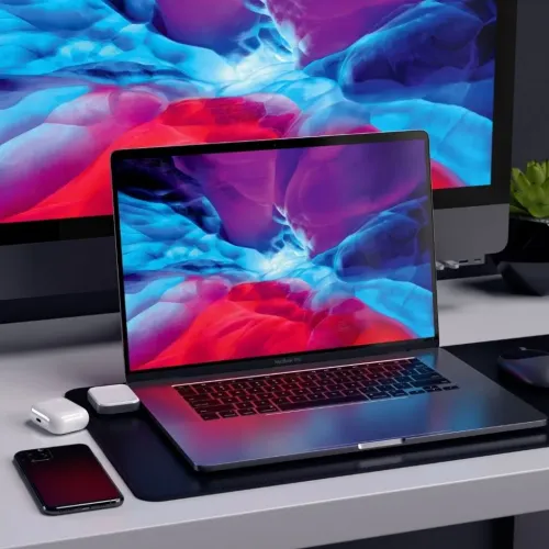 Wireless charging dock for AirPods in low aluminum design, placed next to white AirPods case on desk by laptop.