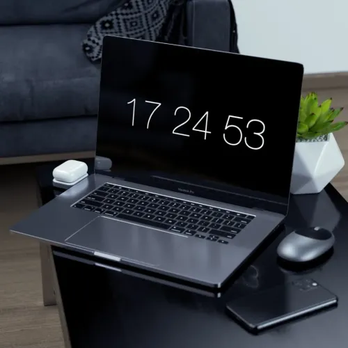 Satechi trådlös laddningsdocka för AirPods bredvid en MacBook Pro på ett skrivbord, med ett vitt laddningsfodral