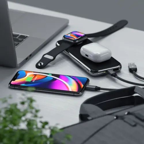 Svart strømbank med ladeflate for Apple Watch; AirPods-etui på toppen, iPhone lades via kabel; synlige LED-indikatorer.
