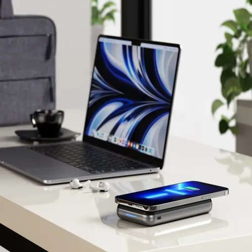 Satechi Duo Wireless Charger Stand charging a smartphone on a desk beside a laptop and earbuds