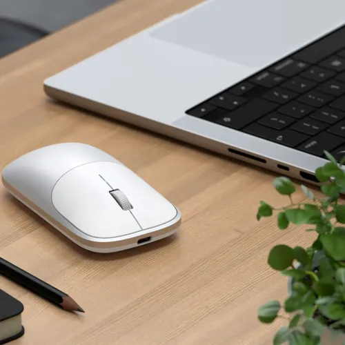 Satechi Slim EX wireless mouse on a desk beside a laptop, showing its compact rounded design and scroll wheel