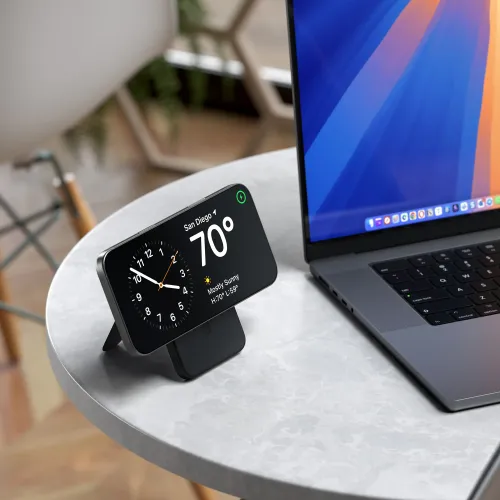 Satechi liten svart powerbank med justerbart stativ holder en smarttelefon horisontalt på et bord, med en bærbar datamaskin ved siden av.