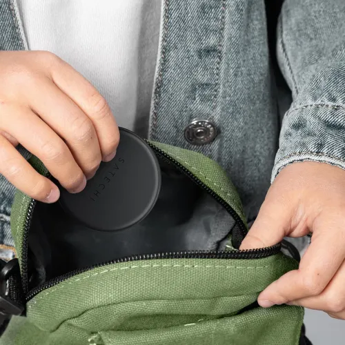 Satechi round portable adapter case in matte black being held above an open green bag