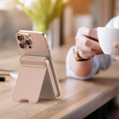 Satechi OntheGo Qi2-magnetisk powerbank med stativ, der holder en rosaguldfarvet smartphone oprejst på et bord