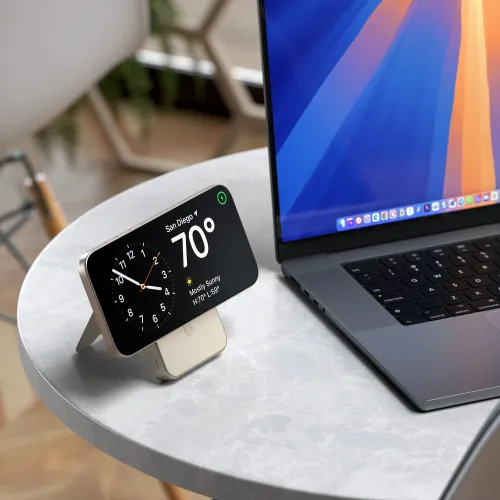 Satechi Qi2 magnetisk powerbank med stativ i sand på rundt bord, utfoldet støtte holder en telefon som ligger ved siden av en bærbar PC.