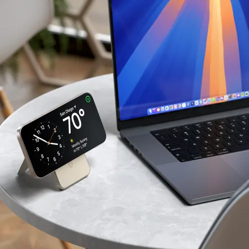 Satechi Qi2 5K magnetisk strømbank med innfelt sandstativ holder en telefon horisontalt på et bord ved siden av en bærbar PC.