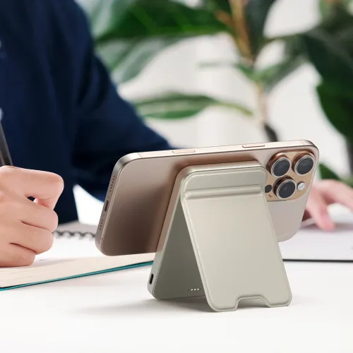 Satechi OntheGo Qi2 magnetinė išorinė baterija su stovu, prilaikanti auksinės spalvos išmanųjį telefoną įkrovimui