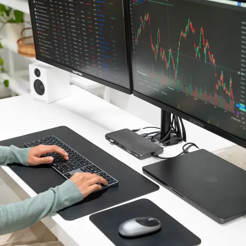 Satechi Thunderbolt 4-dockningsstation på skrivbord under två skärmar, ansluten till laptop, med synliga HDMI- och USB-portar