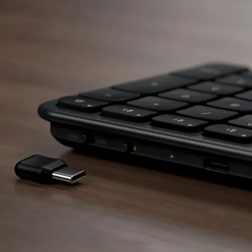 Satechi plona belaidė klaviatūra juodos spalvos su Mac/Win perjungikliu ir USB-C imtuvu ant medinio paviršiaus.