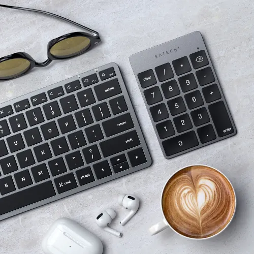 Satechi Slim Keypad, mellomgrått numerisk tastatur med svarte taster og LED, plassert på skrivebordet ved siden av et tastatur.
