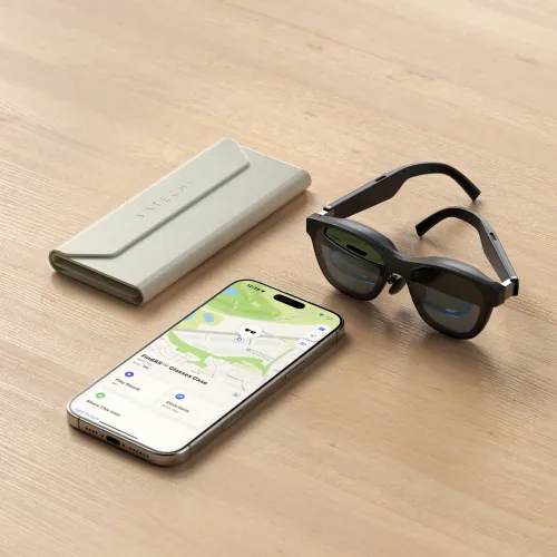 Satechi brilleetui i sandfarget skinnlignende materiale med vinklet klaff, på trebord ved siden av briller og smarttelefon.