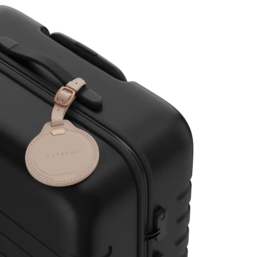 Satechi bagasjelapp i vegansk skinn i Desert Rose med rund form og metallspenne, festet til håndtaket på en svart koffert.